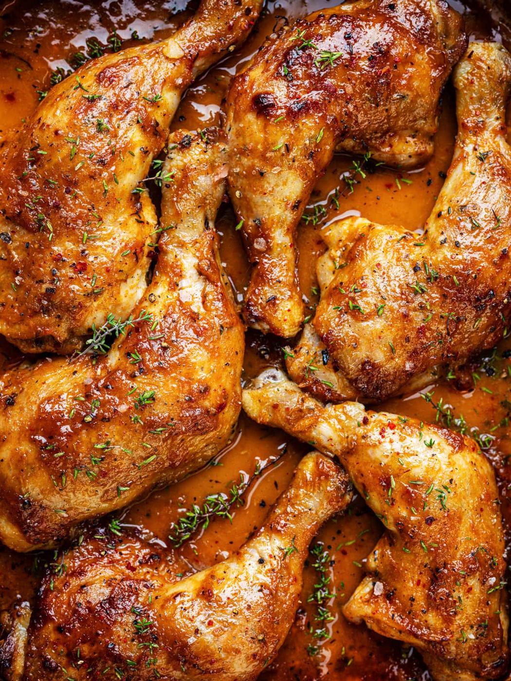 Six golden brown baked chicken leg quarters garnished with fresh herbs and covered in a glossy, seasoned sauce fill the image, creating an appetizing and flavorful presentation.