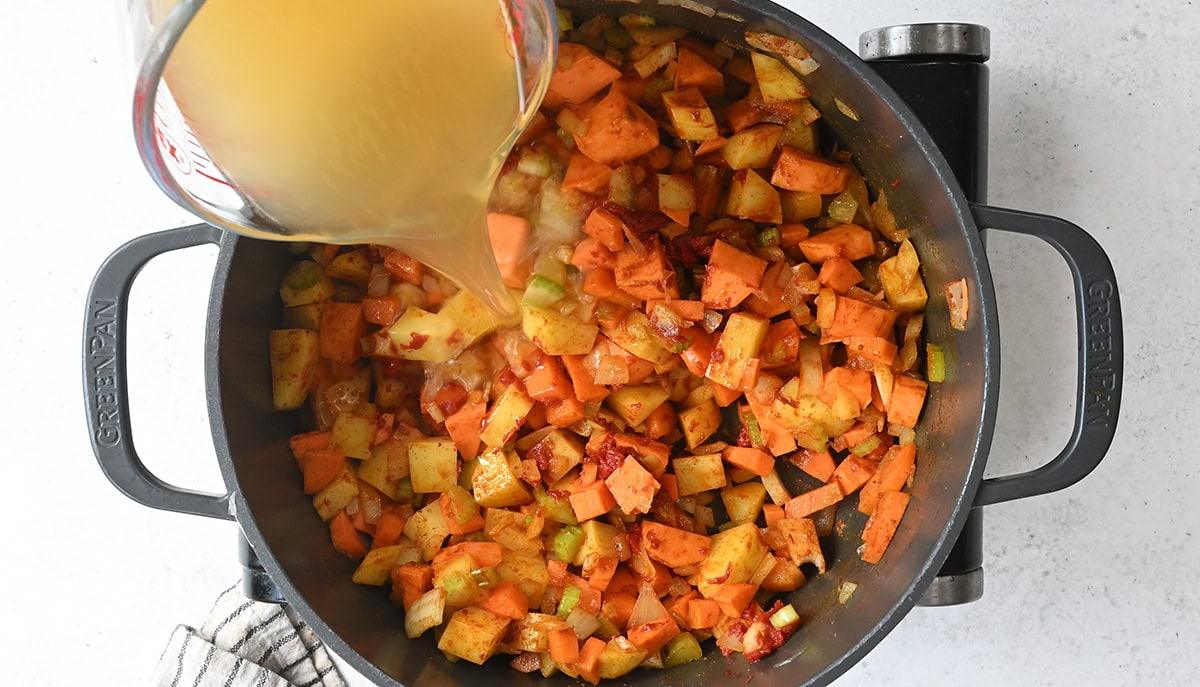 adding chicken broth to pot with sautéed vegetables
