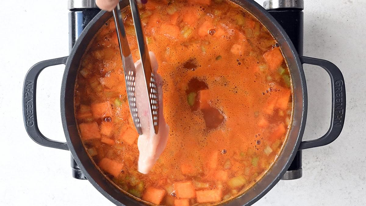 adding chicken breast to a pot of simmering soup