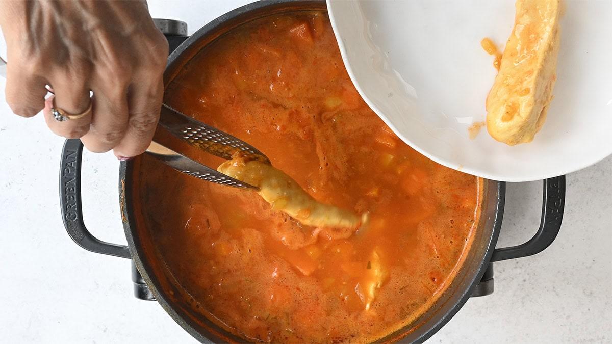 removing cooked chicken breast from soup using tongs