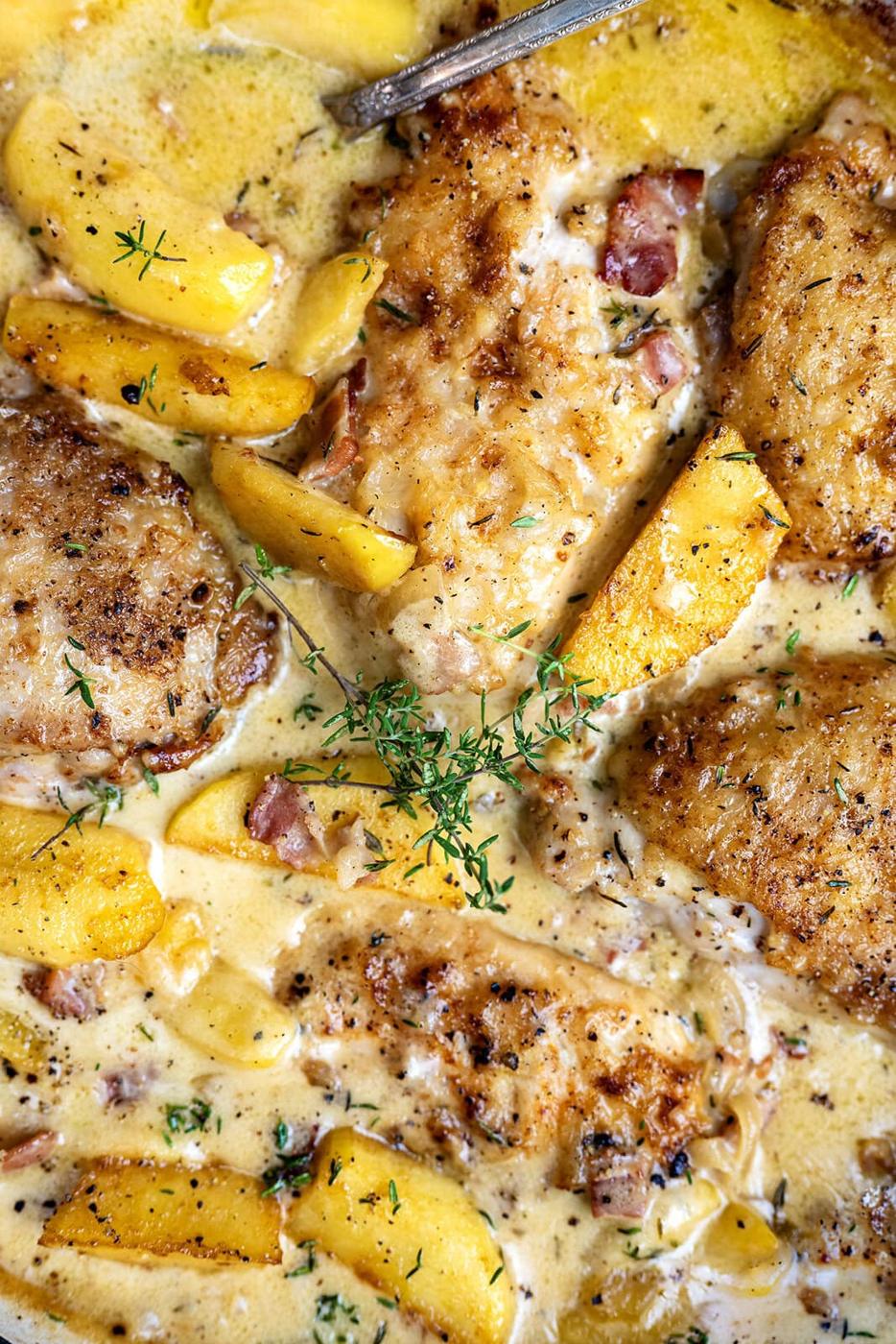 Golden-brown chicken breasts in a creamy sauce with peach slices, bacon bits, fresh thyme, and visible herbs, all garnished with sprigs of thyme—a delightful twist inspired by Chicken Normandy with Cider and Apples.