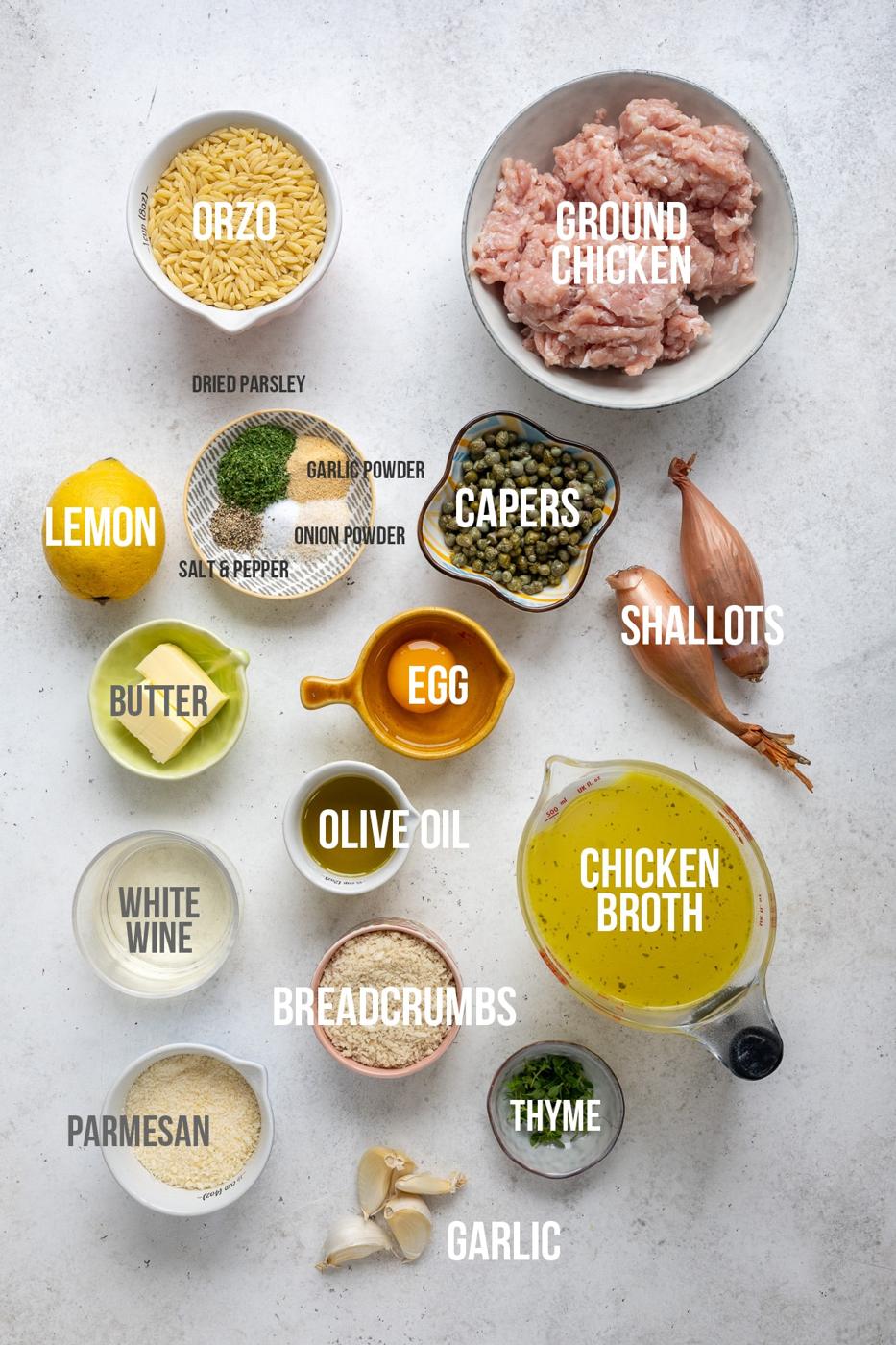 Top-down view of labeled ingredients for Chicken Piccata Meatballs on a white surface, including ground chicken, orzo, capers, shallots, egg, lemon, butter, olive oil, chicken broth, breadcrumbs, parmesan, garlic, thyme, and seasonings.
