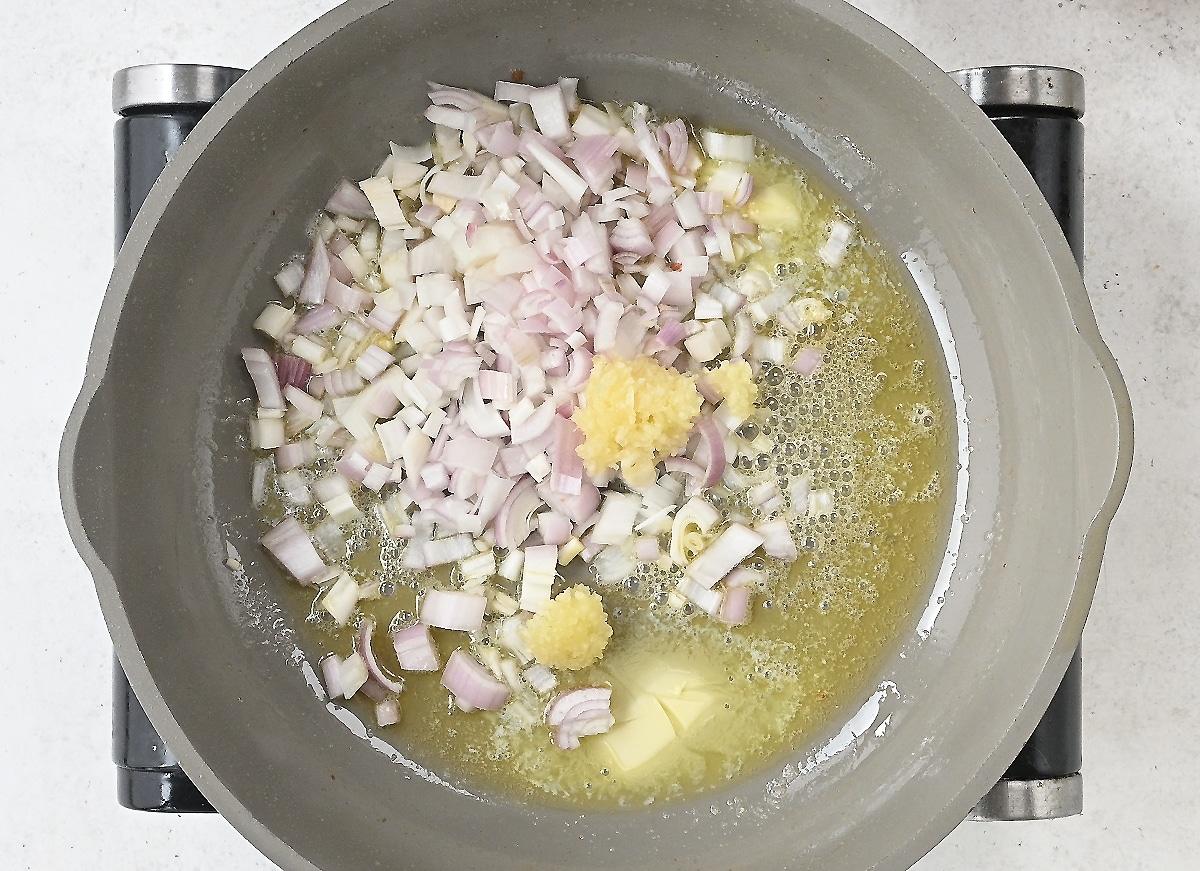 Chopped onions and minced garlic cooking in melted butter in a gray pan on a stovetop, forming the savory base for Chicken Piccata Meatballs.