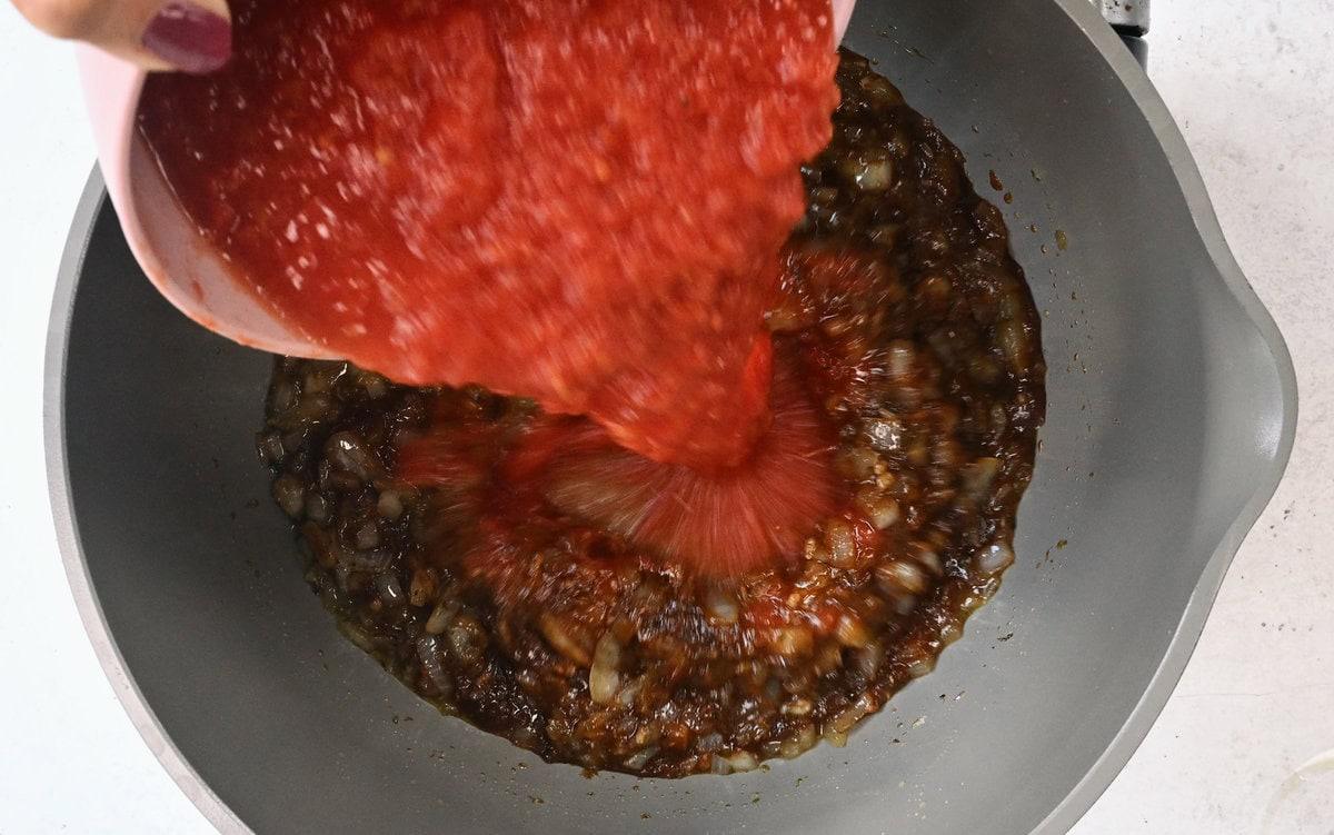 adding tomatoes to a Dutch oven for chicken tinga sauce