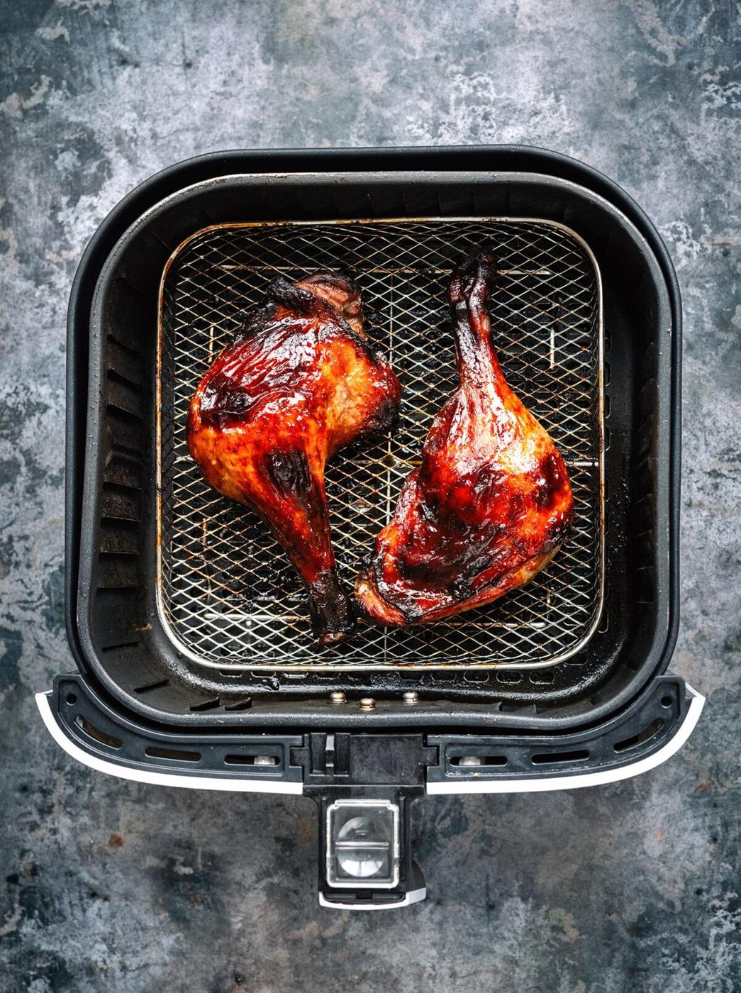 Two glazed, roasted duck leg quarters sit in the basket of an air fryer