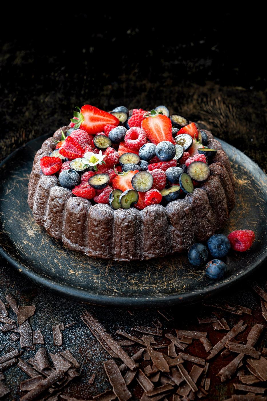 Chocolate almond cake with chocolate ganache and fresh berries on a wooden platter