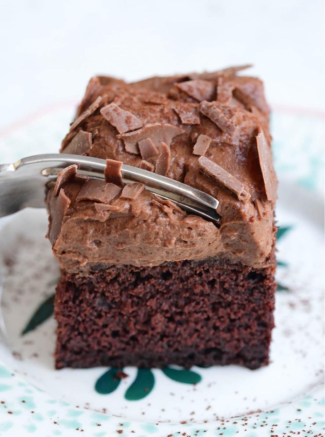 Slice of chocolate banana cake with chocolate frosting on a plate with a form cutting through