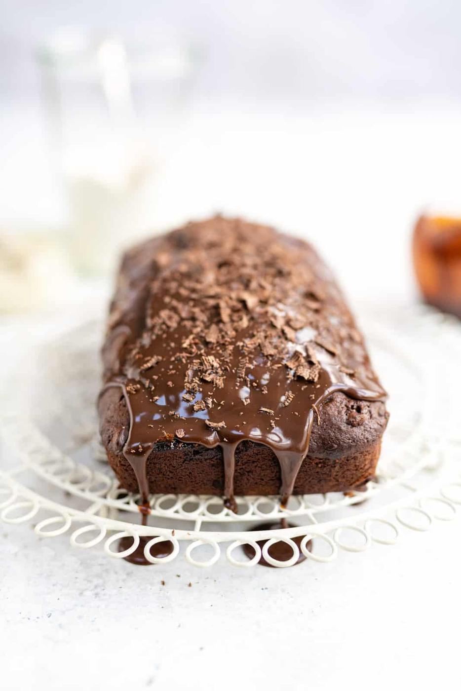 Chocolate banana cake covered with chocolate glaze and chocolate shavings on a white wire cooling rack