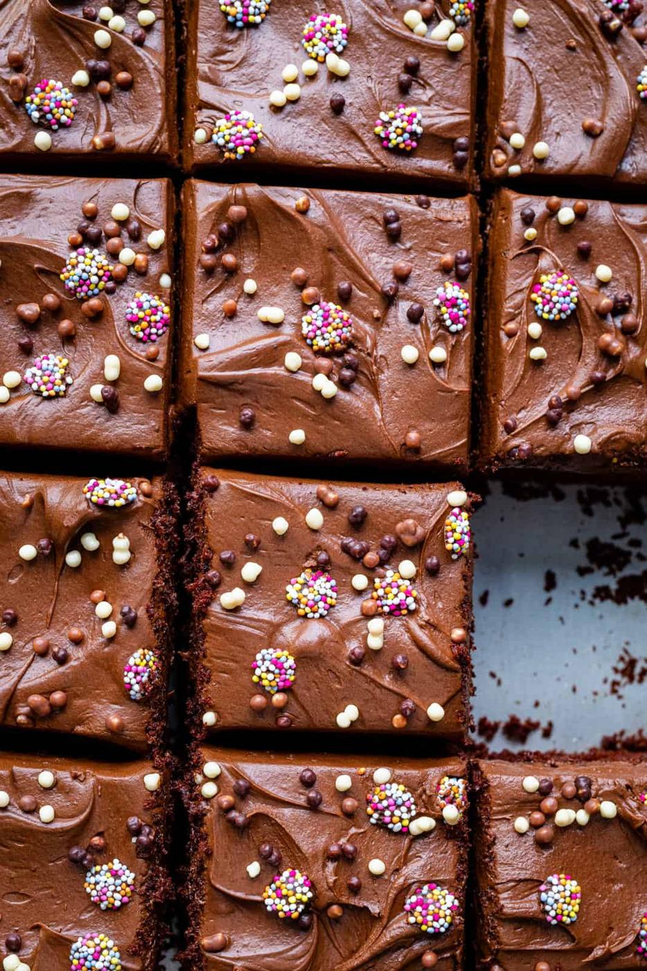 close up on a chocolate sheet cake covered in chocolate frosting and sprinkles and cut into squares