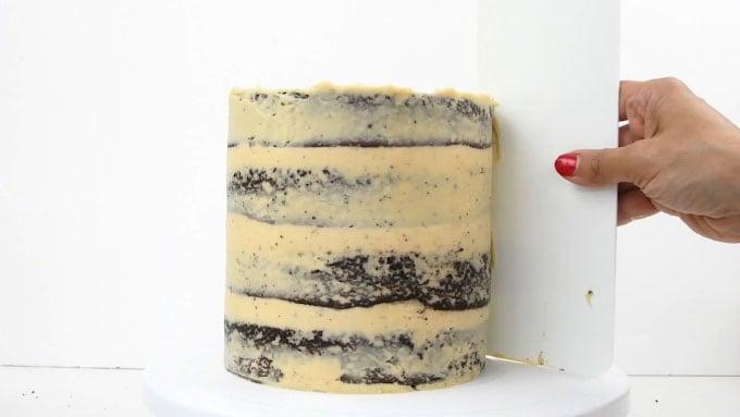 Smoothing frosting on a tall chocolate caramel layer cake with side scraper