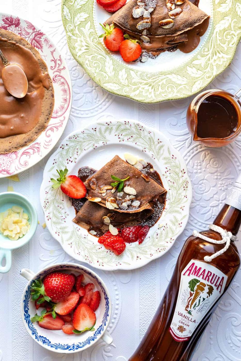 three plates with chocolate pancakes filled with Nutella, strawberries and drizzled with chocolate sauce