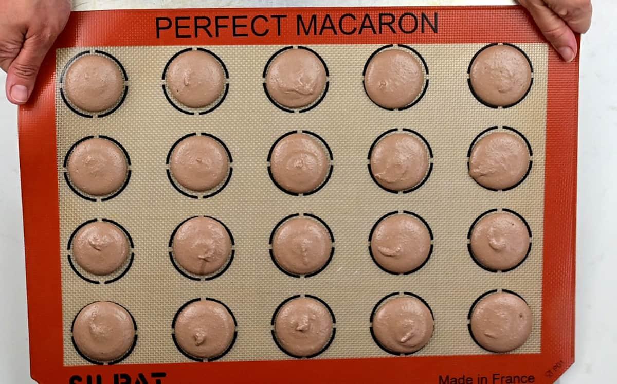 tapping a tray of chocolate macarons against kitchen counter to release air bubbles