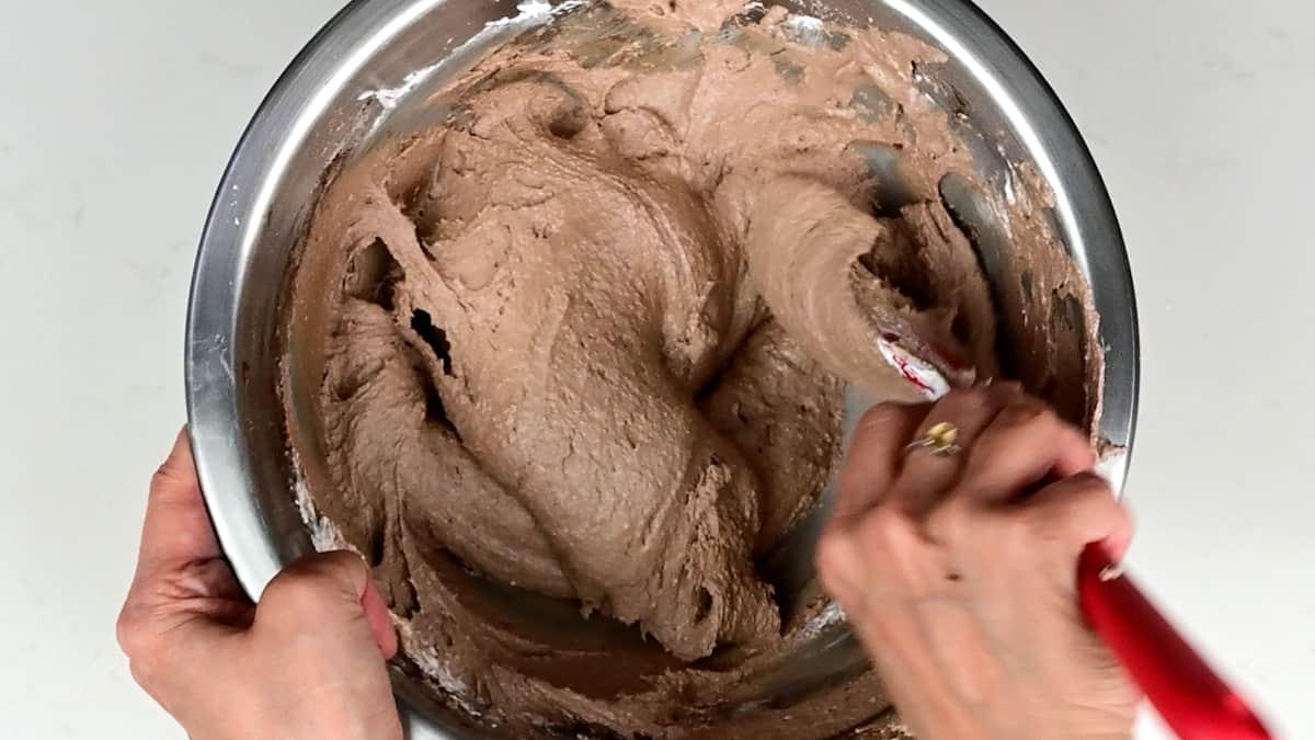 folding meringue into almond paste to make macarons in a bowl