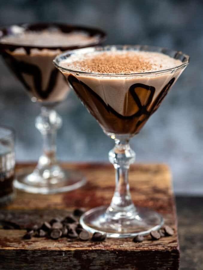 Two martini glasses decorated with chocolate syrup and filled with chocolate cocktail