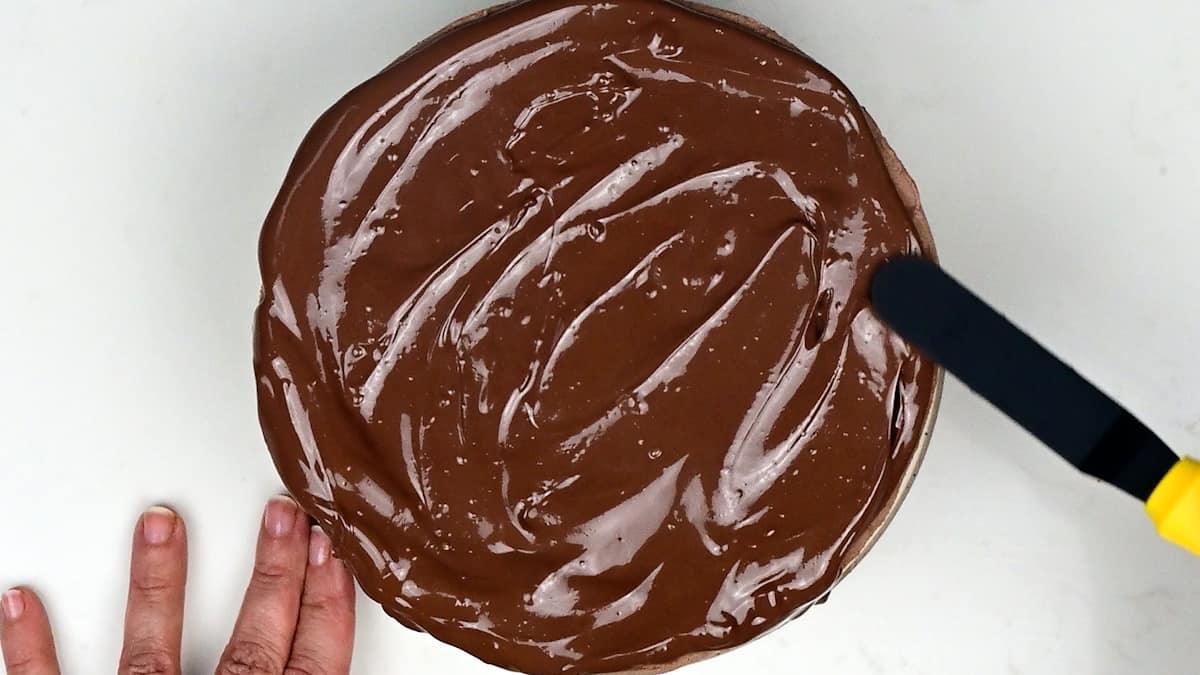 spreading melted chocolate over cheesecake