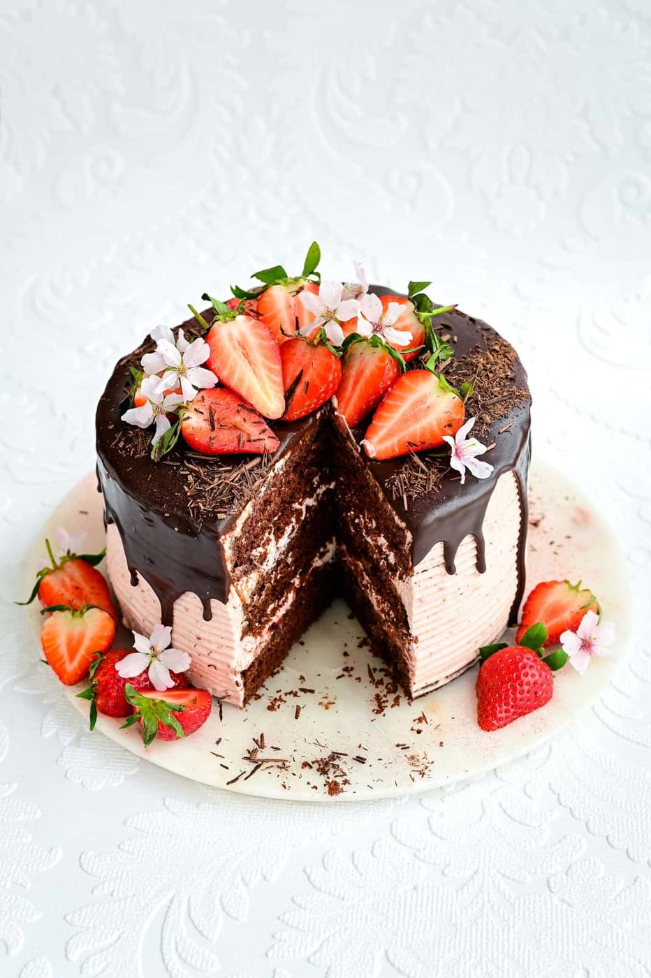 Chocolate strawberry layer cake on a marble platter with slice cut out