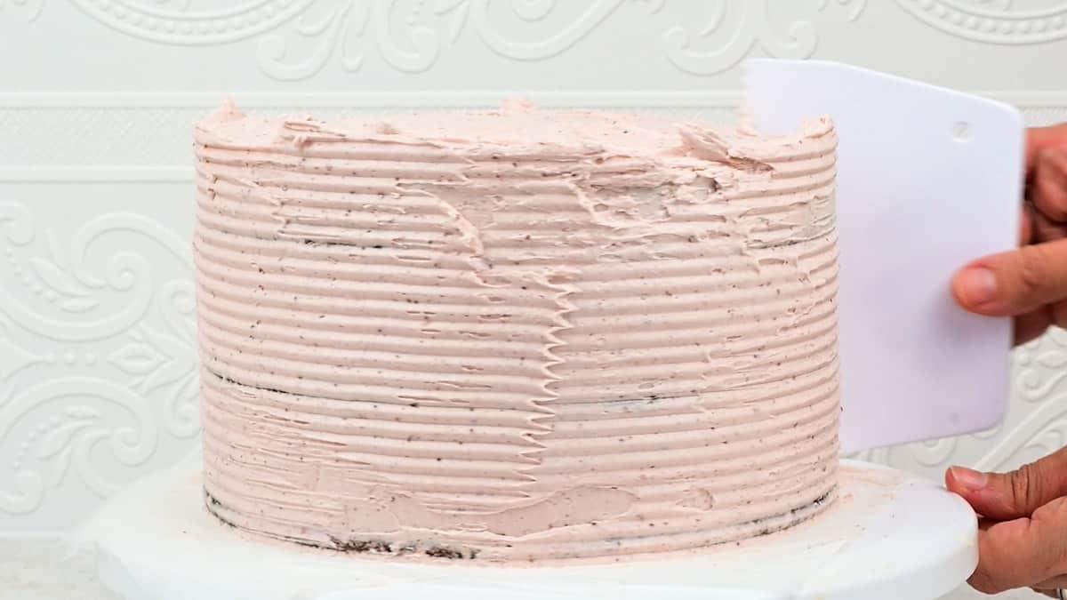 using a sawtooth bench scraper to create pattern on side of layer cake