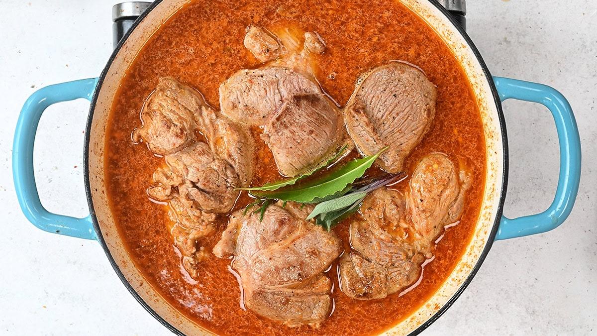 pork shoulder pieces in apple cider and broth in a casserole dish