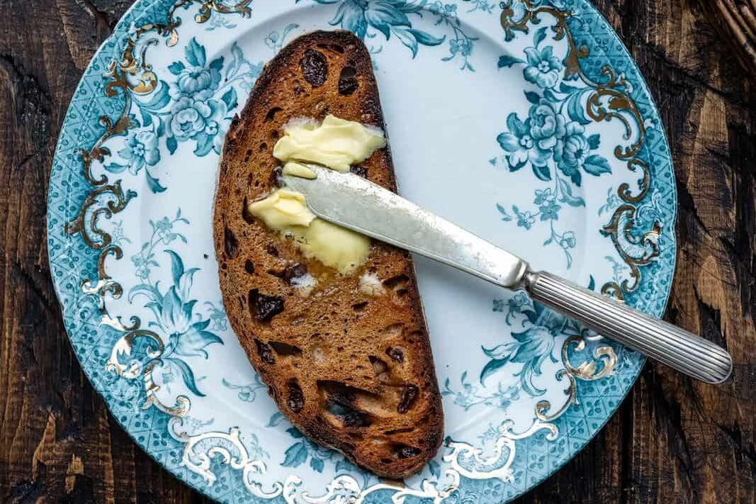Slice of sourdough cinnamon raisin bread spread with butter on a vintage plate