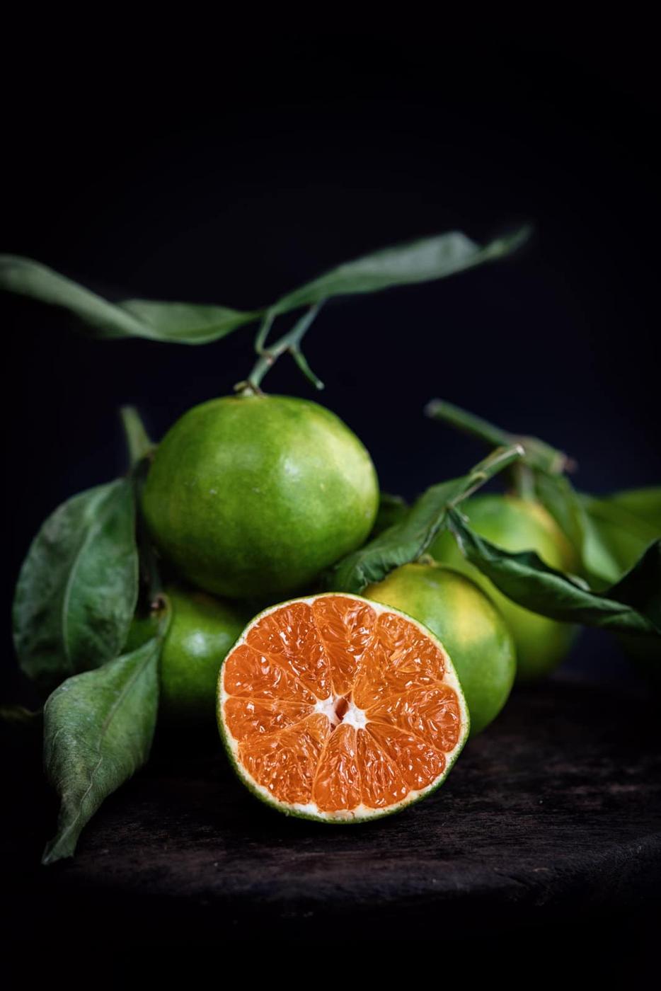 Green skinned mandarins, one sliced to show bright orange flesh