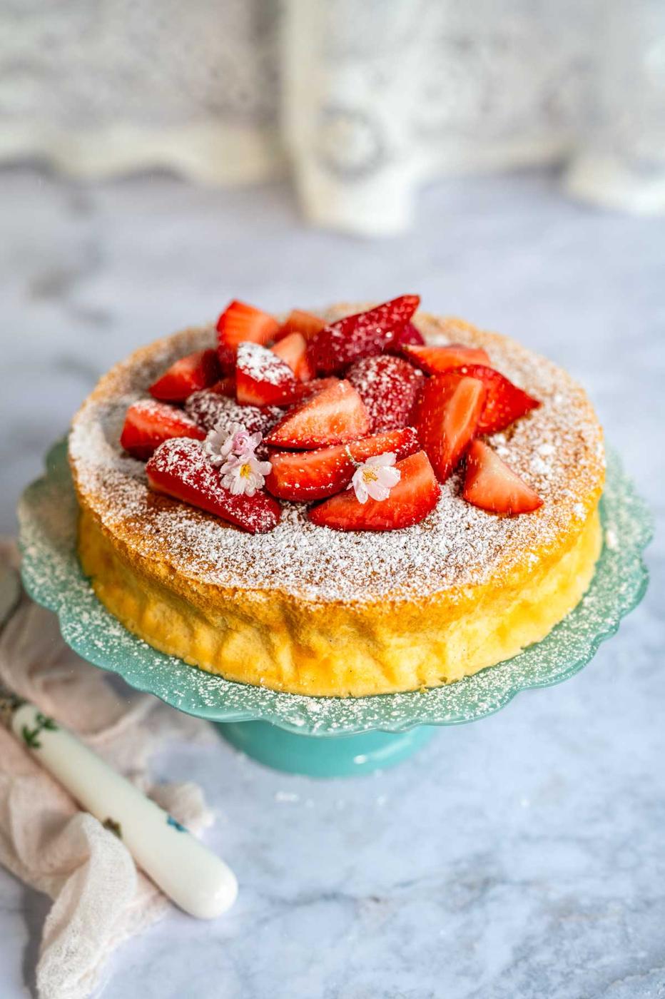 cloud cake on a stand topped with sliced strawberries and powdered sugar