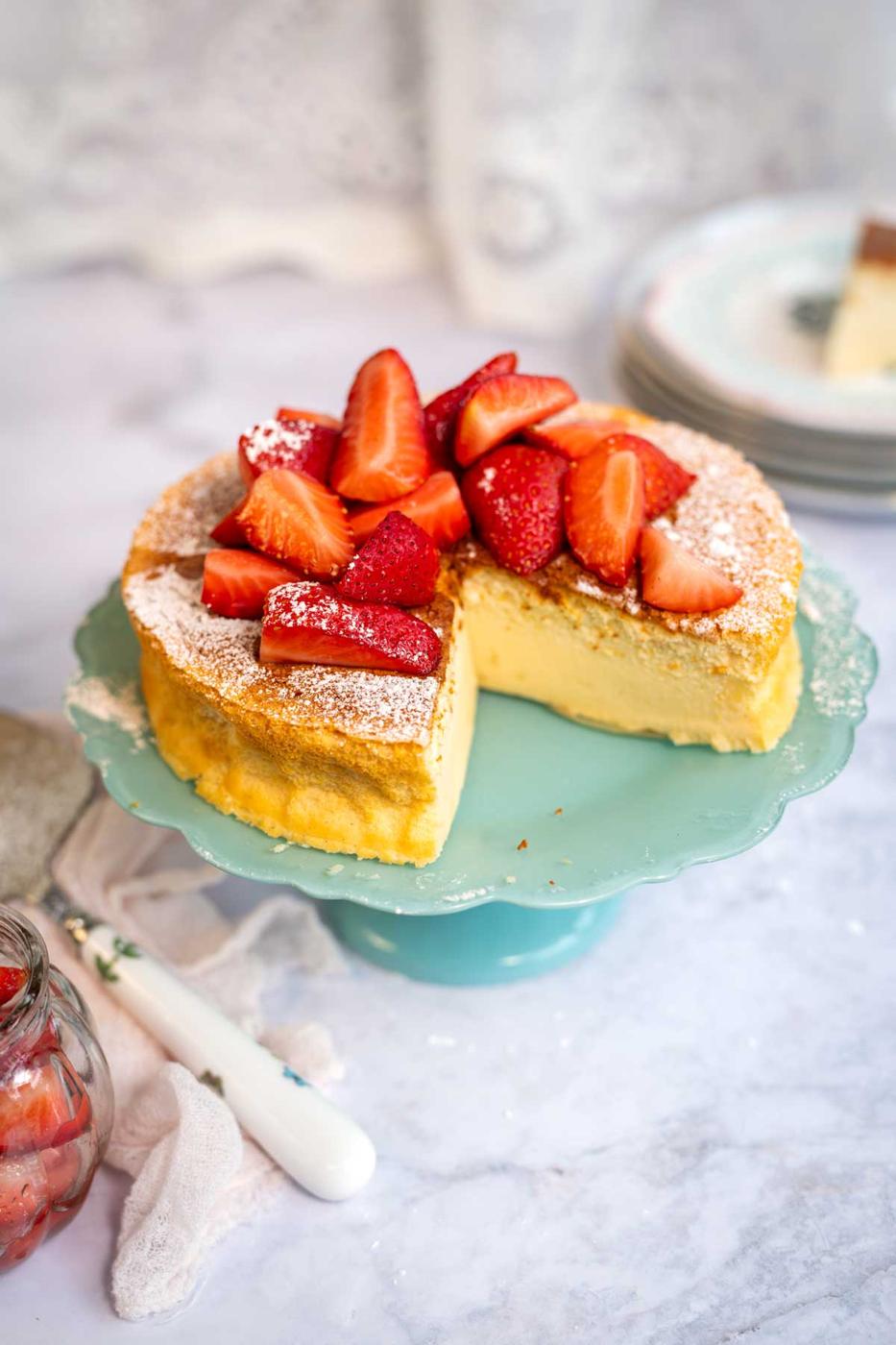 Vanilla cloud cake with a large slice cut on a stand, plates in the background