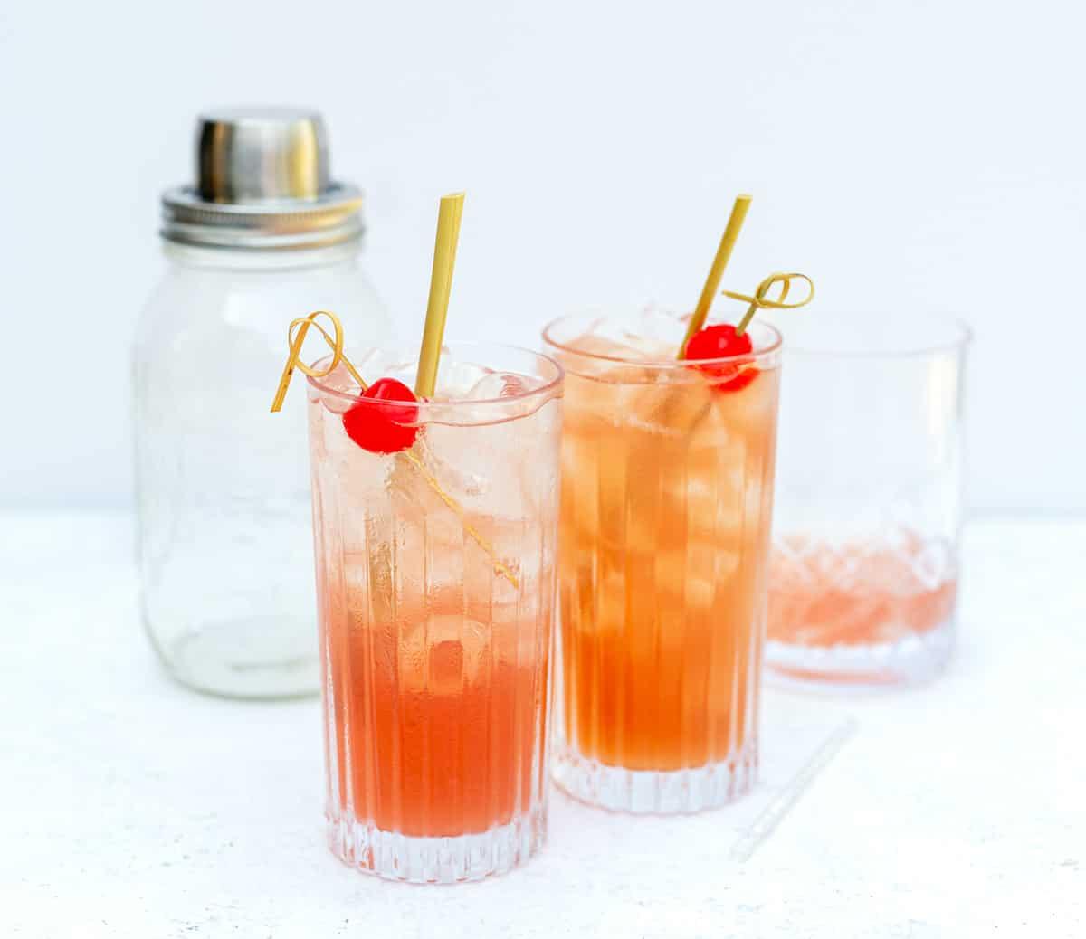 Two servings of Singapore Sling drinks in tall glasses garnished with cocktail cherries