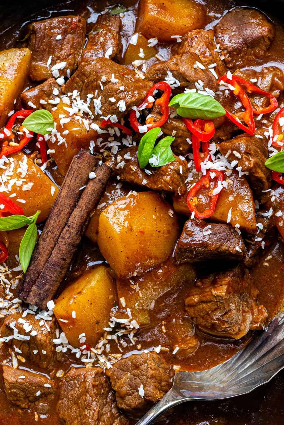close up on a bowl of Beef curry garnished with sliced chilli and basil leaves