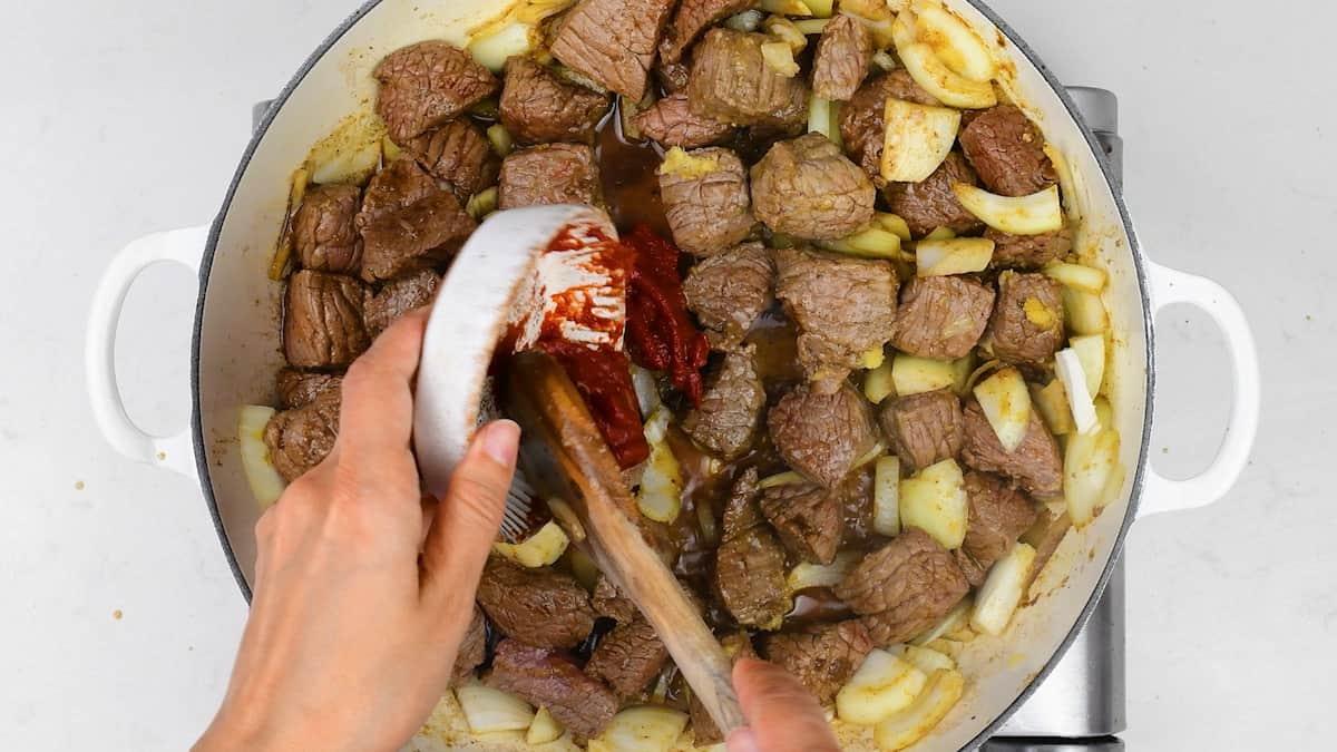 adding tomato paste to a pot with beef and onions