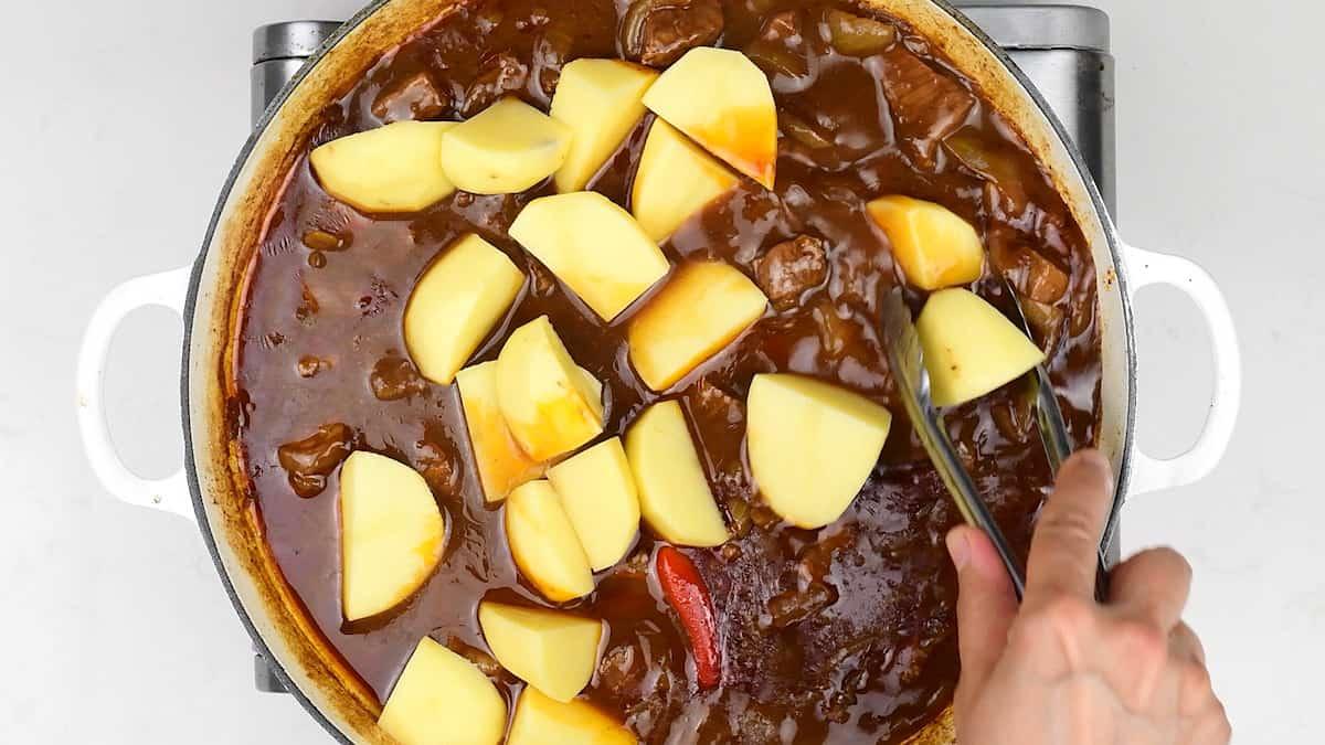 adding cubed peeled potatoes to a beef curry