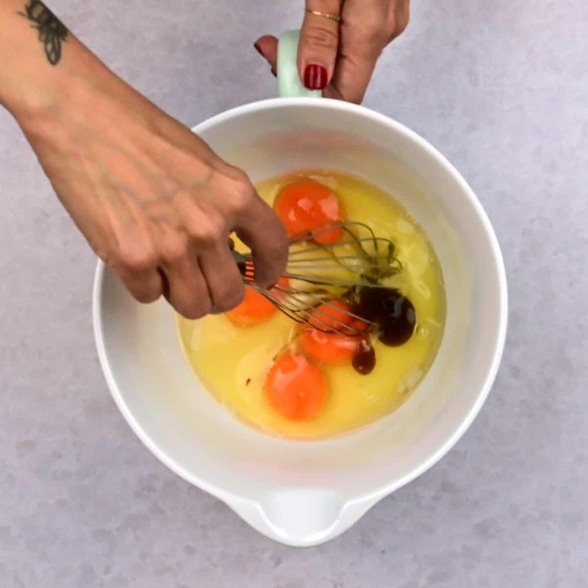 stirring eggs with condensed milk and vanilla in a bowl