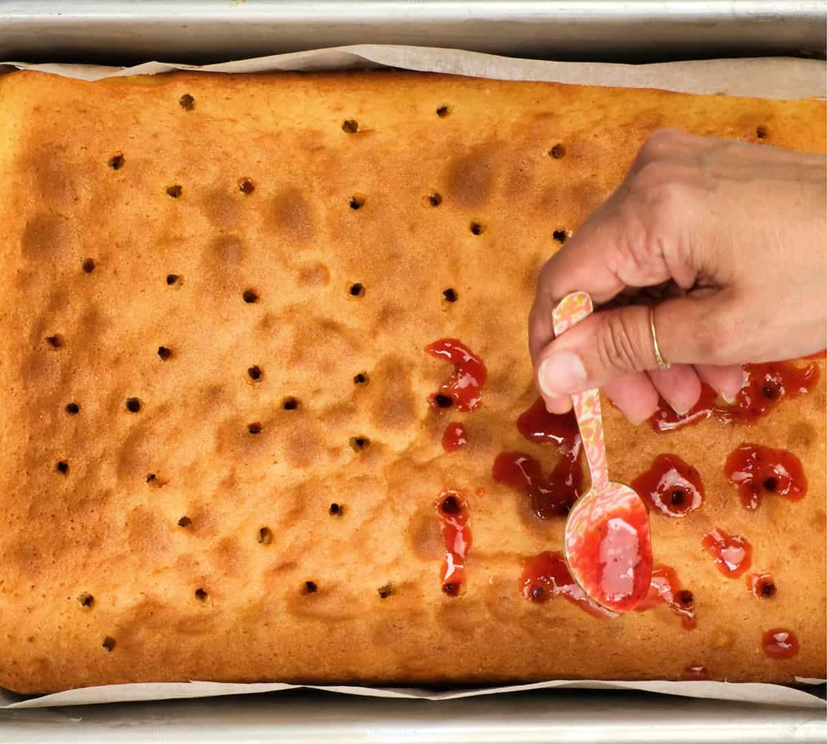 poking holes and spreading jam over sponge cake
