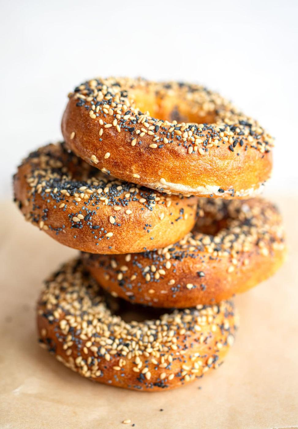 A stack of four golden-brown cottage cheese bagels topped with sesame seeds and black poppy seeds, placed on parchment paper against a light background.