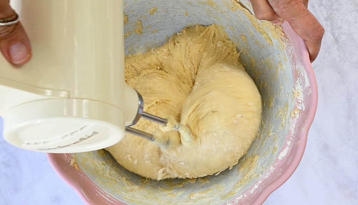 kneading bread dough in a bowl using a hand mixer