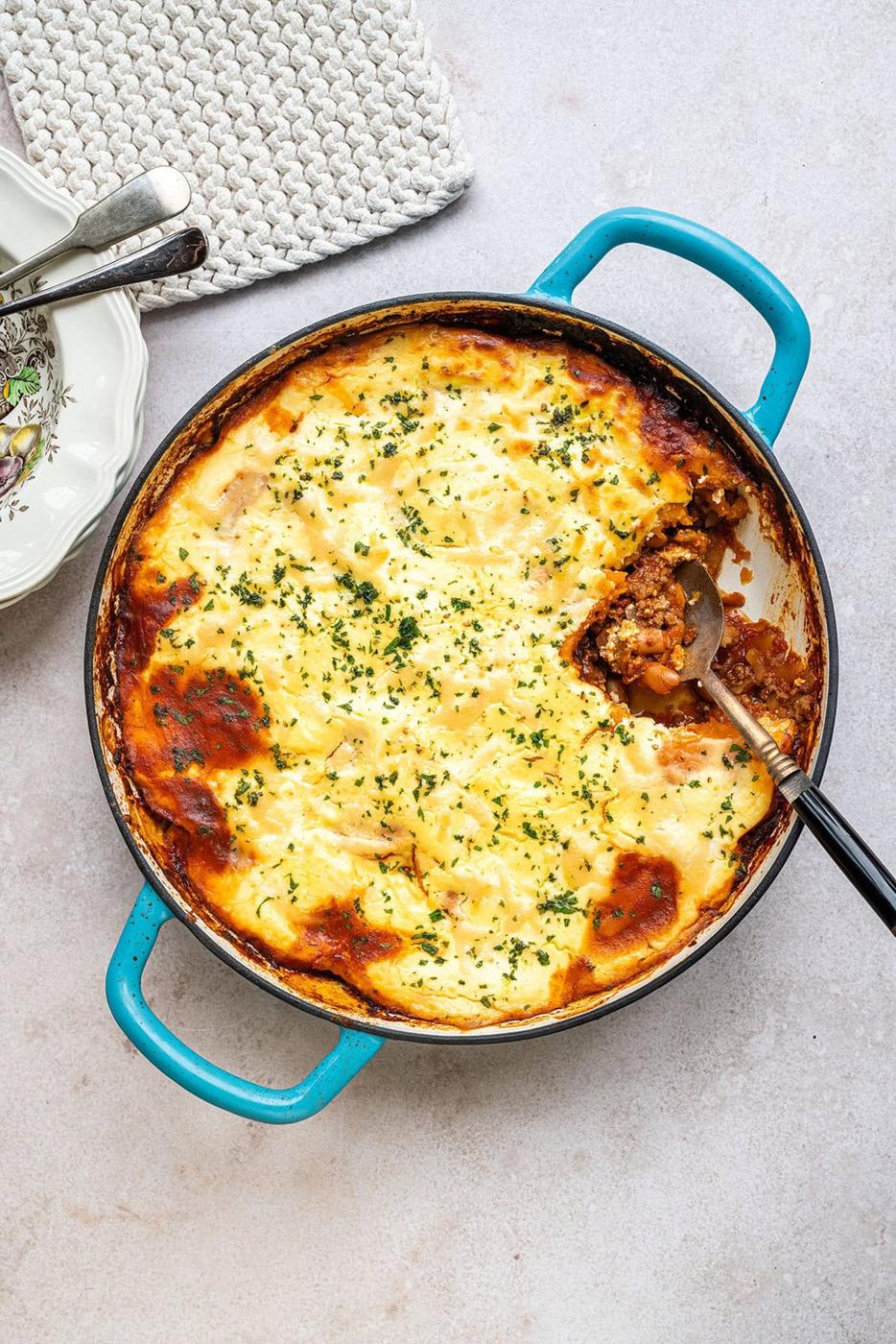 A round blue baking dish filled with ground beef, topped with roasted sweet potatoes and topped with cottage cheese. A portion has been scooped out