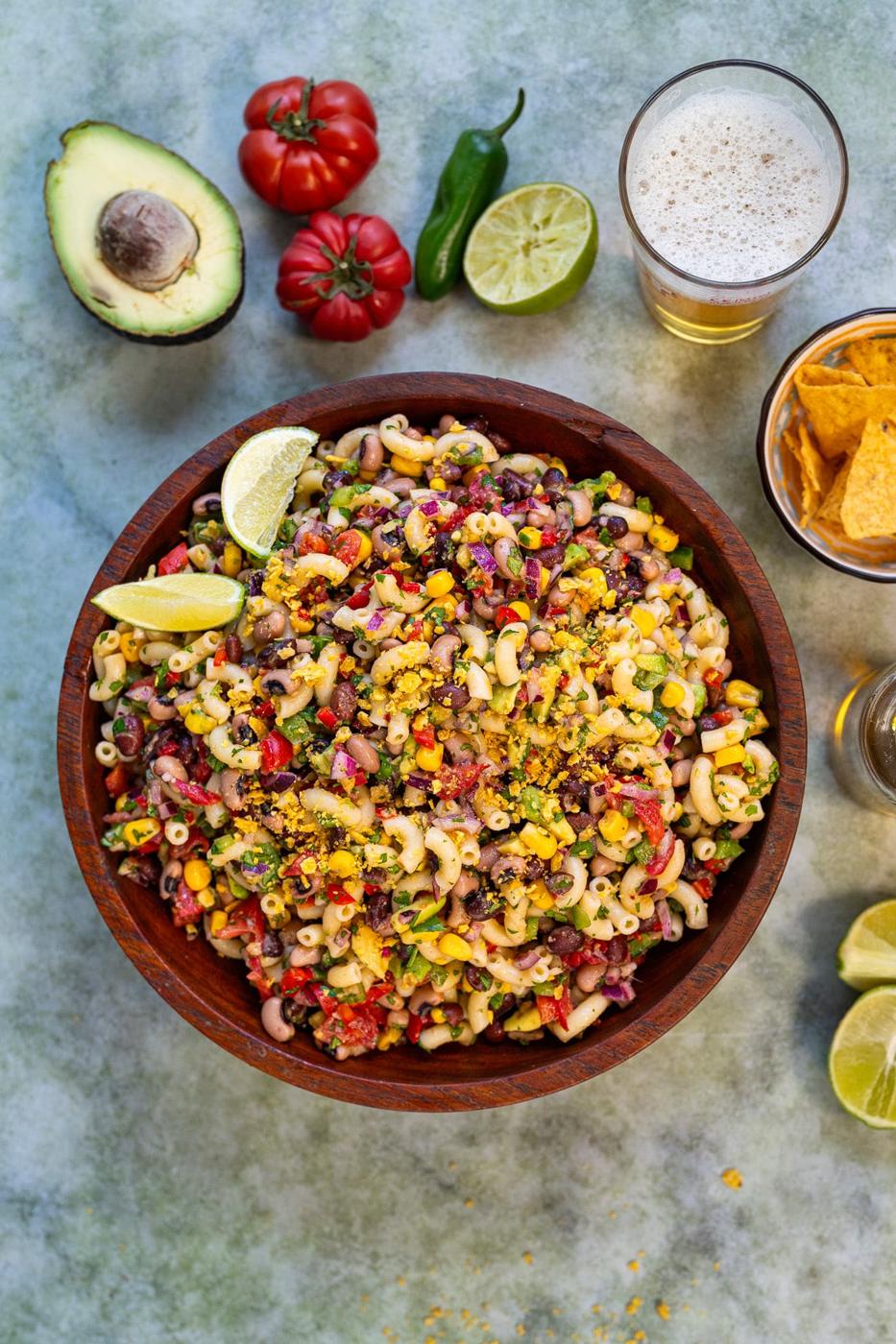 A bowl of Cowboy Caviar Pasta Salad with assorted vegetables and tortilla chips on the side.