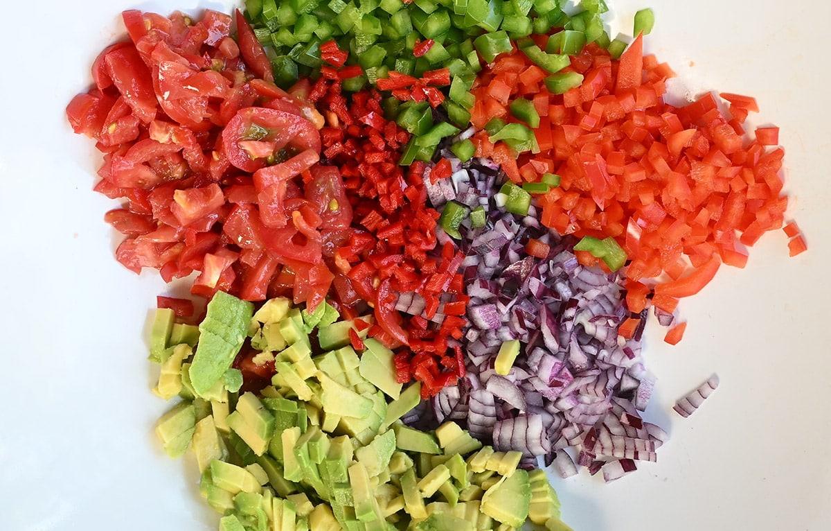 close up on a bowl of finely chopped tomatoes, peppers, onion, avocado and jalapeno