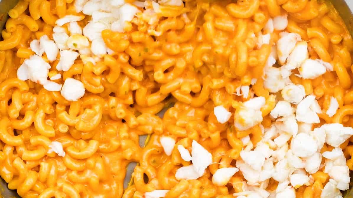 stirring crab meat into macaroni and cheese in a pan
