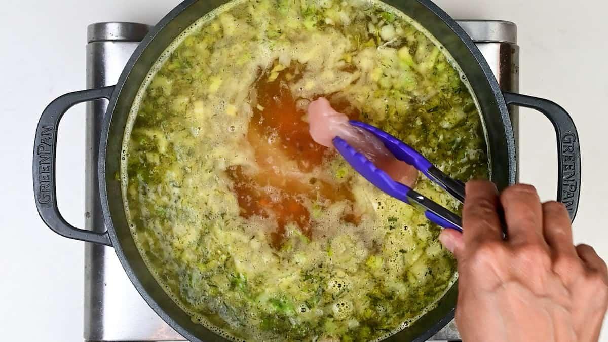 adding chicken breasts to pot of soup