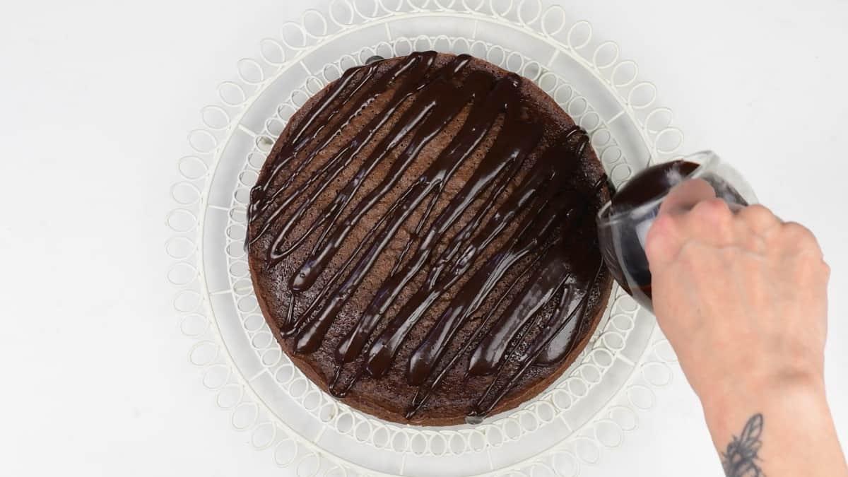 pouring chocolate glaze over chocolate cake placed on wire rack