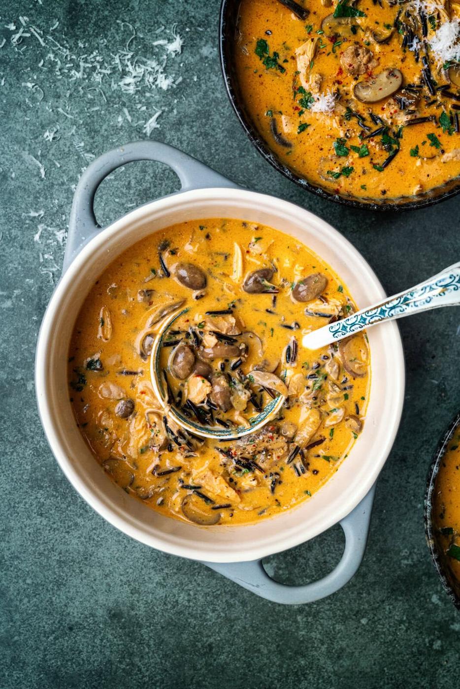 creamy chicken and wild rice soup with mushrooms in a small ceramic pot with ladle in the soup.