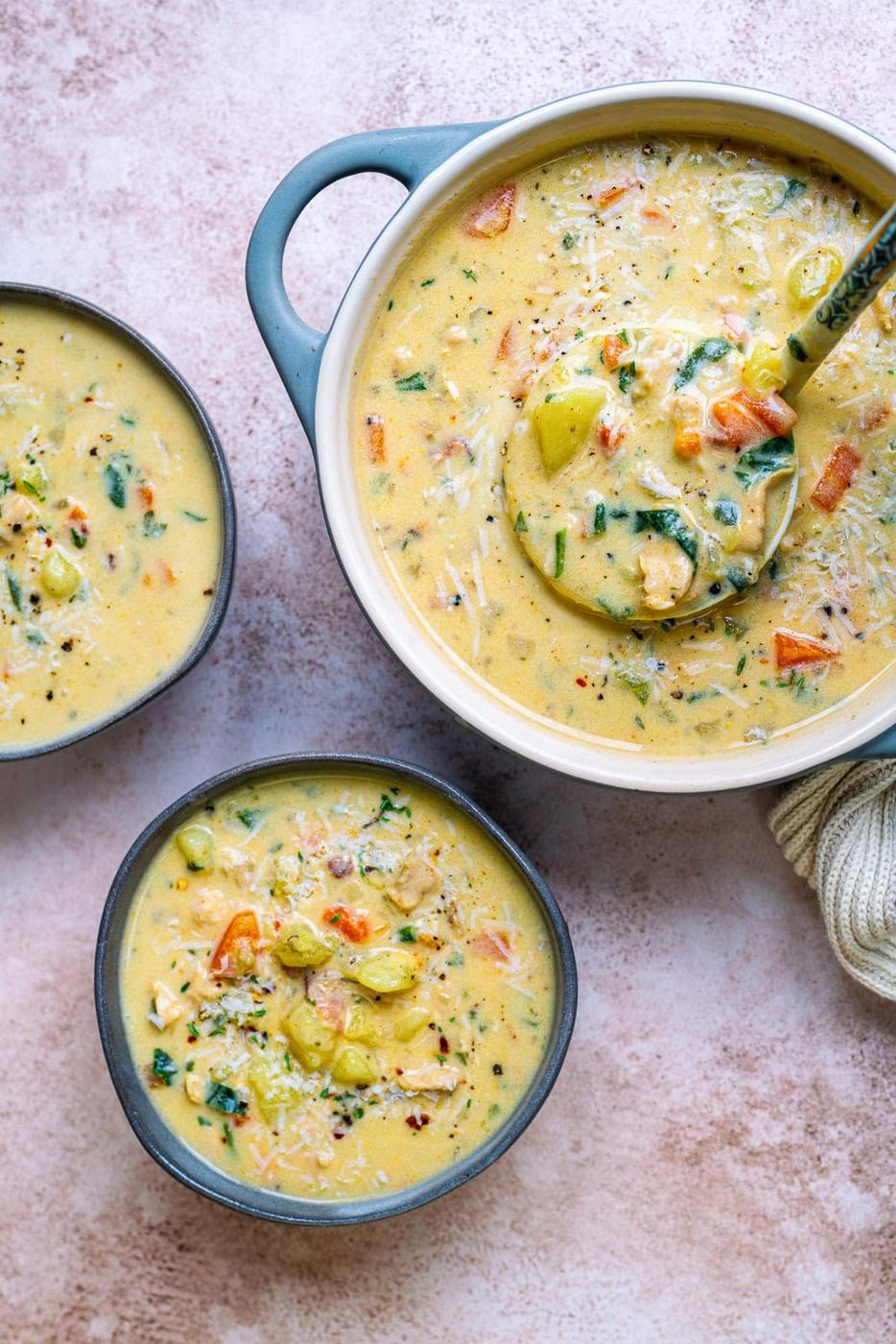 pot of creamy chicken potato soup with two small bowl servings on the side