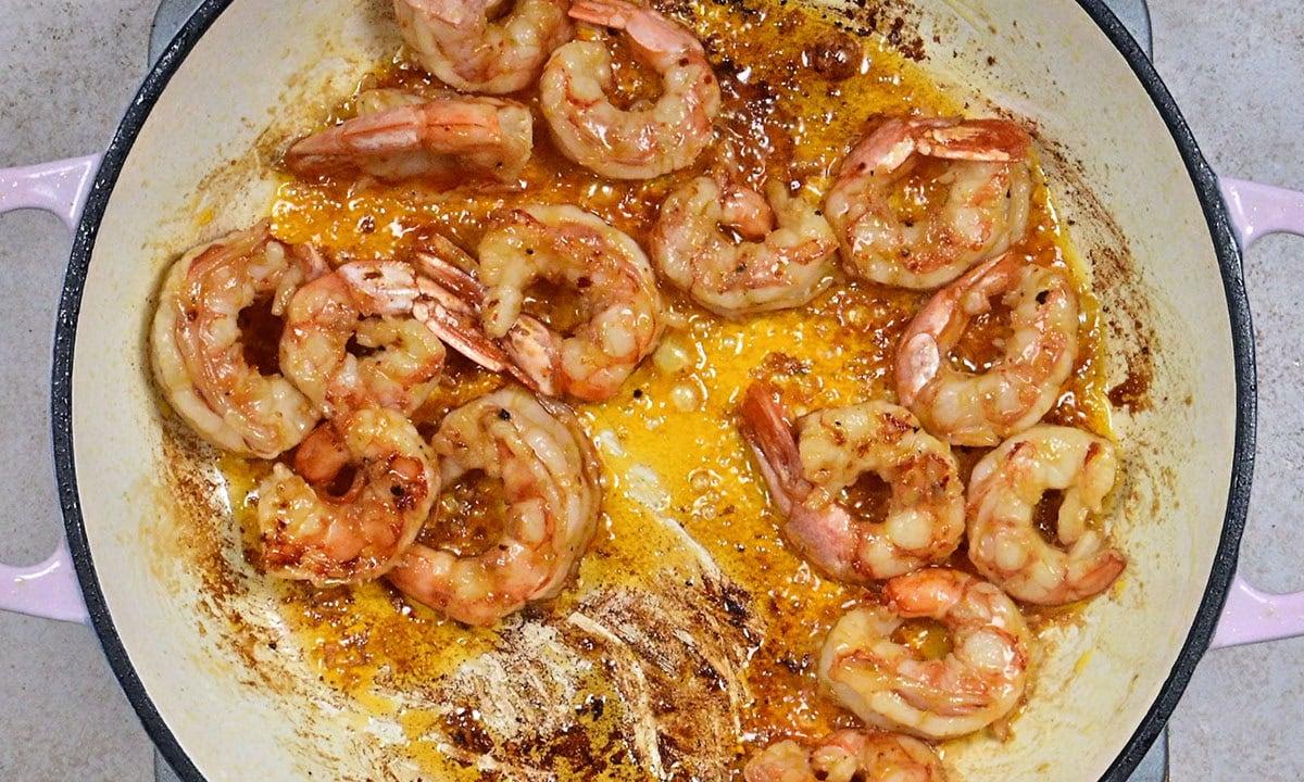 Shrimp cooking in a round pan with a golden, seasoned sauce; some browning on the pan and shrimp, indicating they are being sautéed.