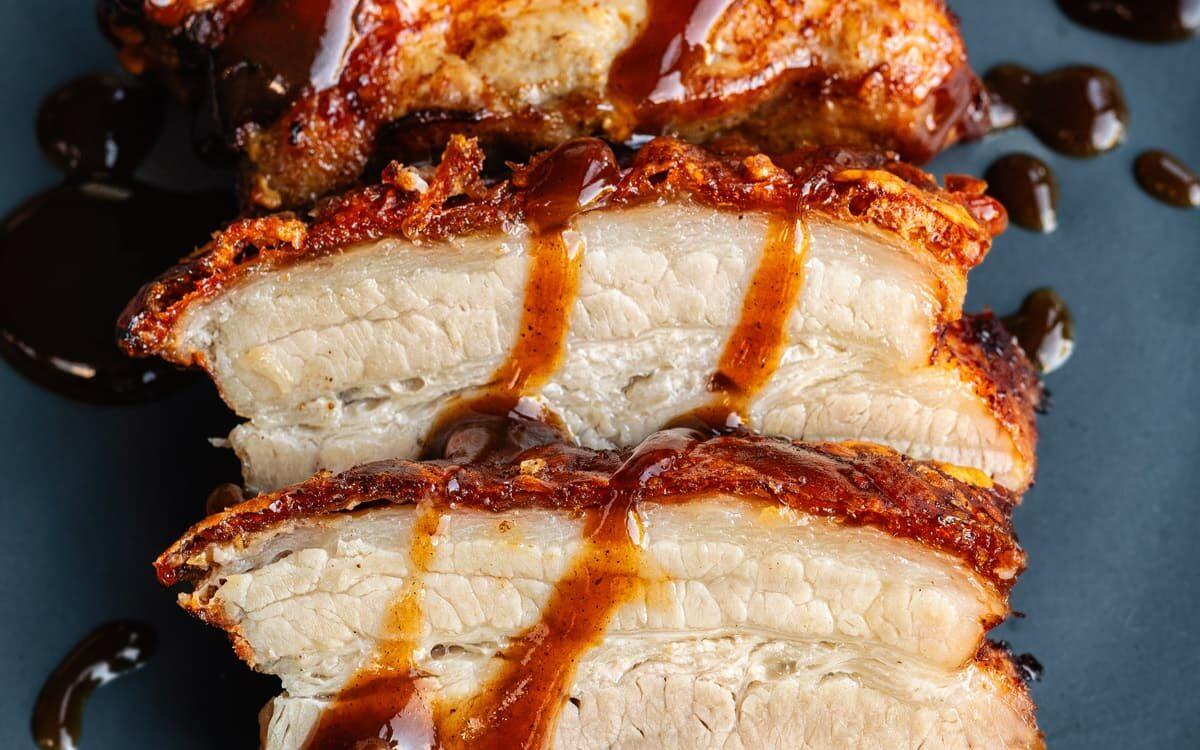 Crispy air fryer pork belly, sliced on a blue plate and drizzled with sauce