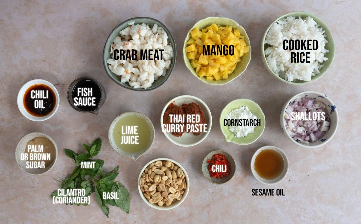 Bowls containing crab meat, mango, cooked rice, chili oil, fish sauce, lime juice, Thai red curry paste, cornstarch, shallots, palm or brown sugar, mint, cilantro, basil, peanuts, chili, and sesame oil.