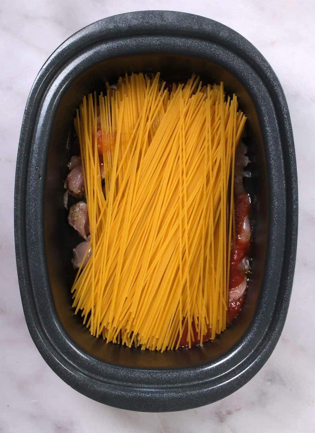 Dry spaghetti noodles in a slow cooker on top of tomato sauce and diced chicken