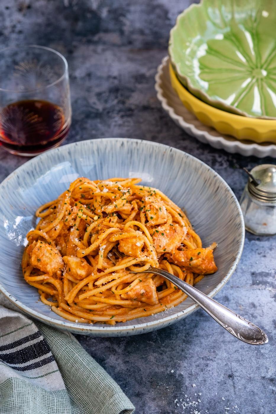 Bowl of creamy chicken spaghetti in a tomato sauce, bowls stacked in the background