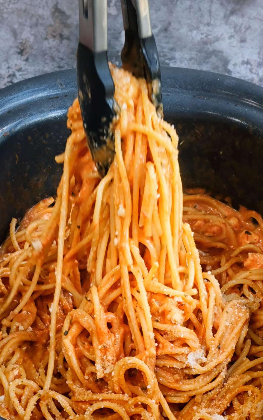 Tongs tossing spaghetti in a slow cooker