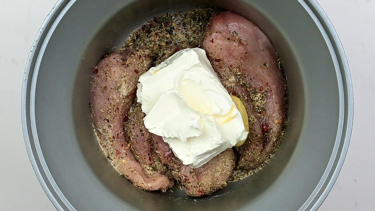 seasoned chicken breasts topped with cream cheese in a slow cooker