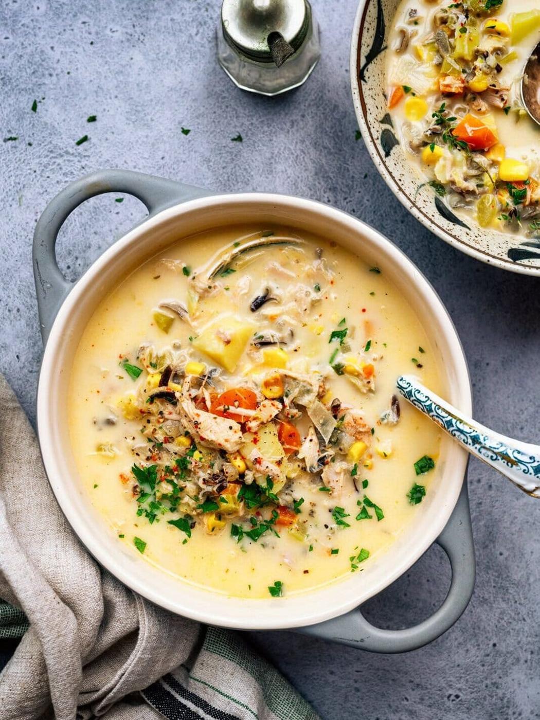 Overhead photo of crockpot turkey soup in a small ceramic pot, a bowl serving of the soup on the side